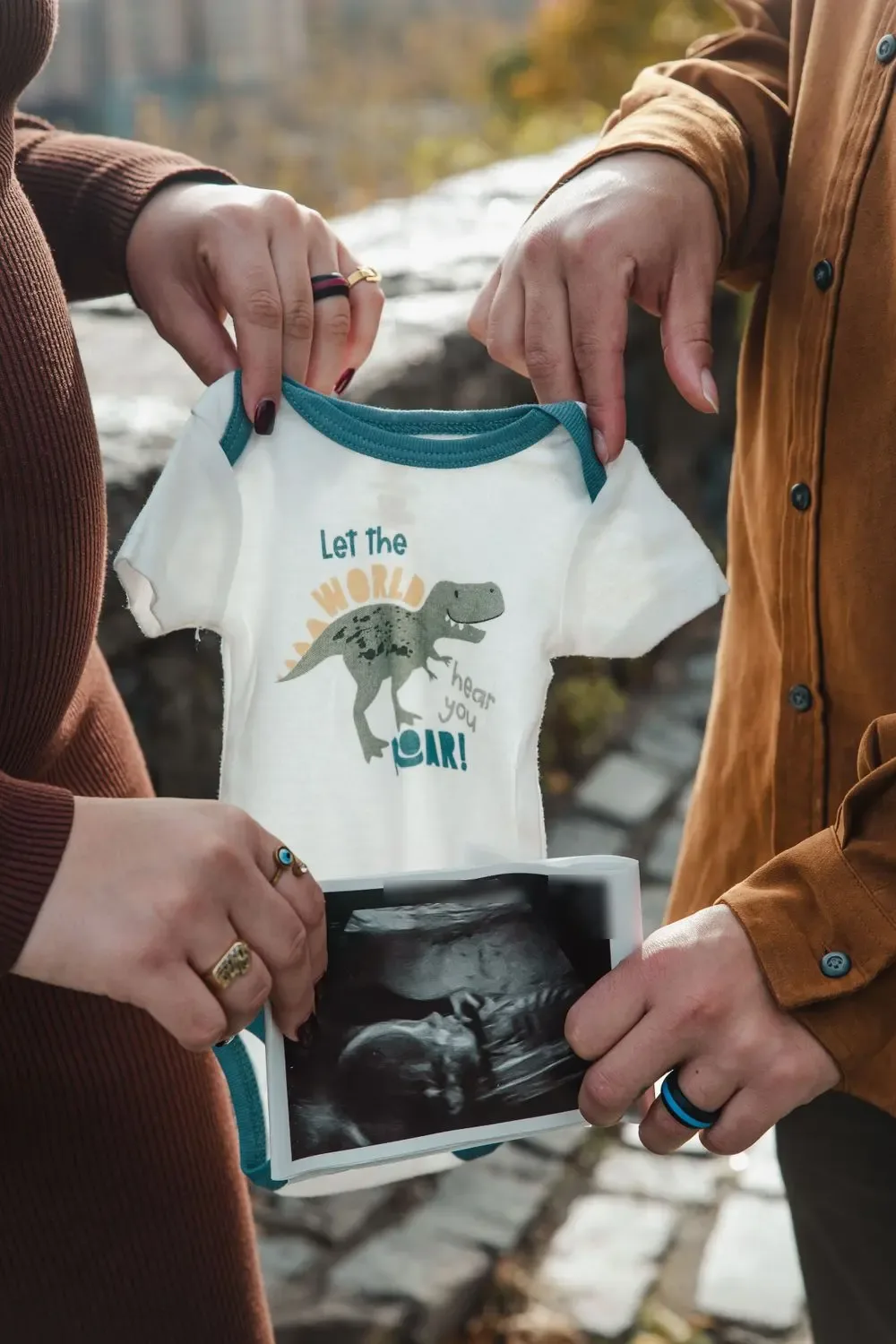 Expecting parents holding a dinosaur onesie and a sonogram print for a pregnancy announcement photo by Create With Amy, a Maryland maternity photographer