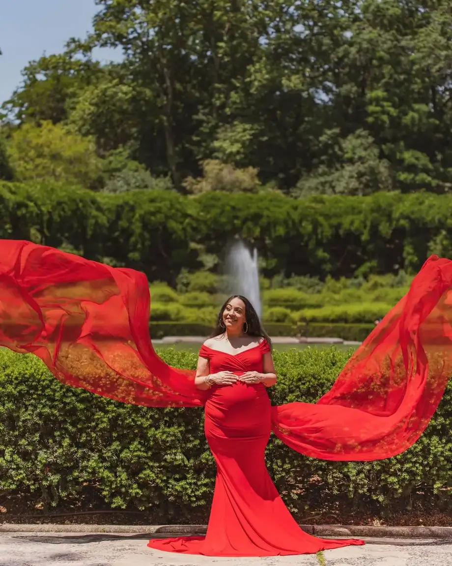 Expecting mother in a red maternity gown with the long train thrown into the air in a formal garden, photographed by Create With Amy, Baltimore maternity photographer