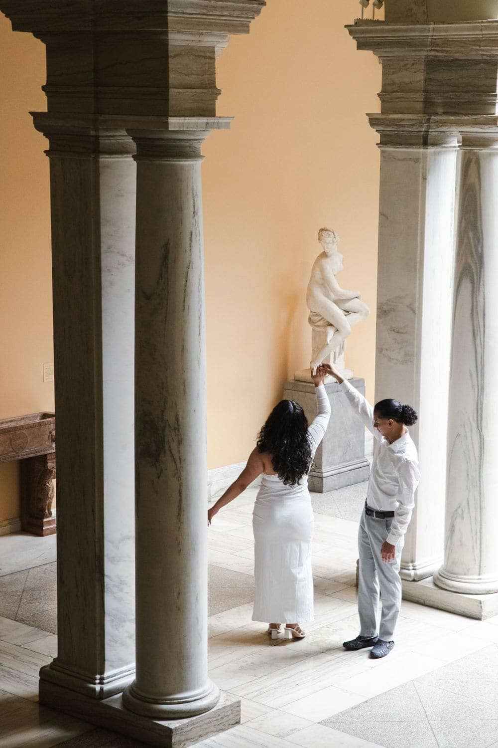 Couple dancing between marble columns during an engagement photo session by Create With Amy in Baltimore, Maryland